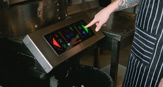 Person in an apron clicking a green arrow on a large touchscreen display