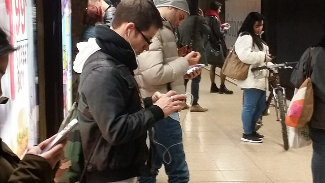 A group of people in a public space using their smartphones, perhaps to access a mobile e-signature solution