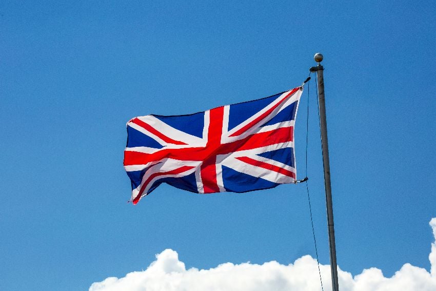 The Union Jack atop a flagpole seen against a blue sky with fluffy white clouds
